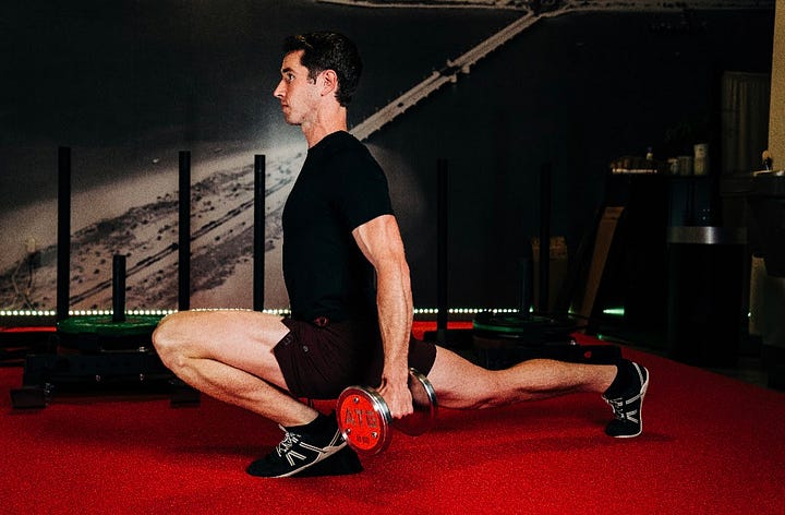 A man on a red carpet completing a lunge with weights.